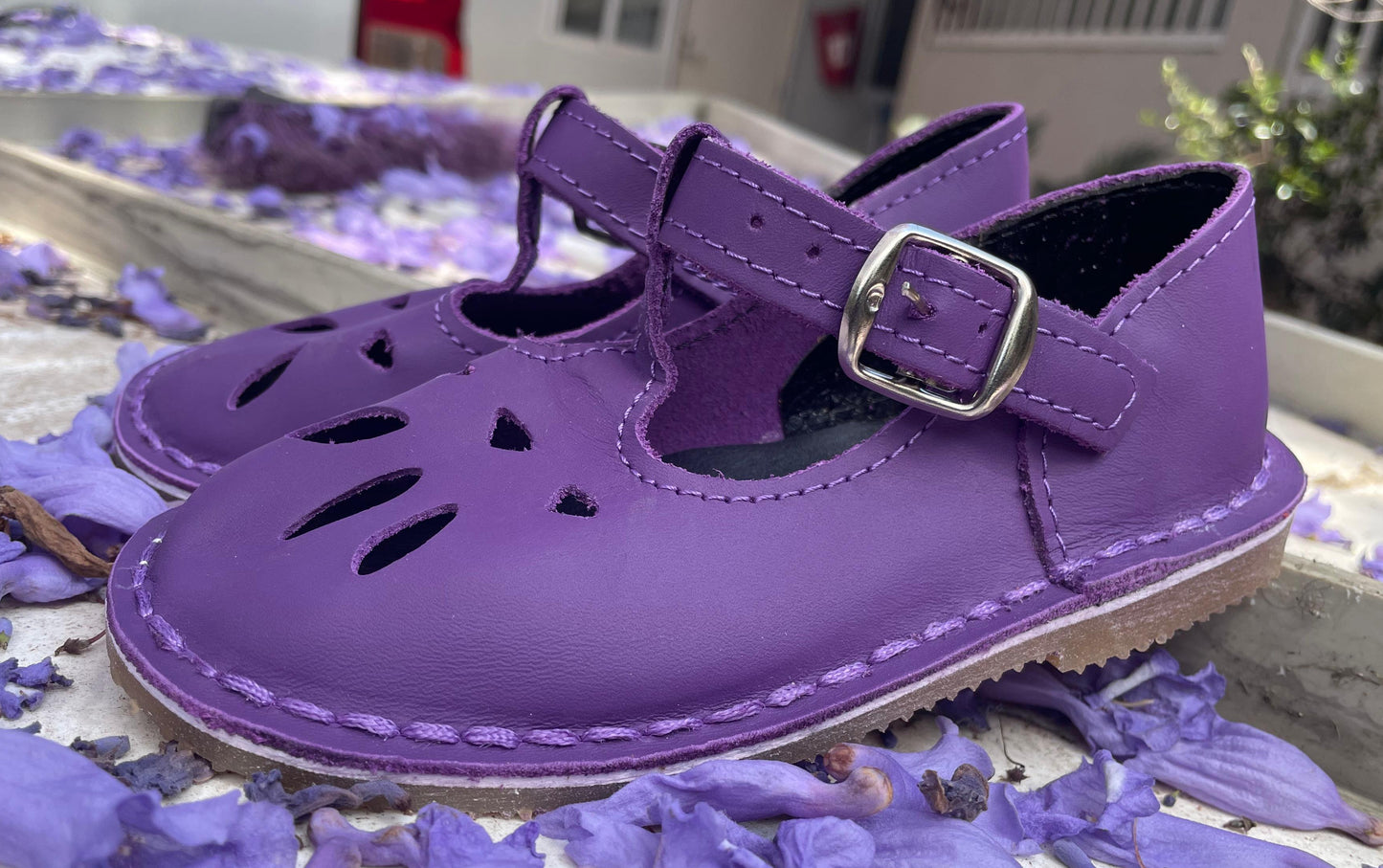 Purple children's shoes with a buckle on a surface with purple flowers.