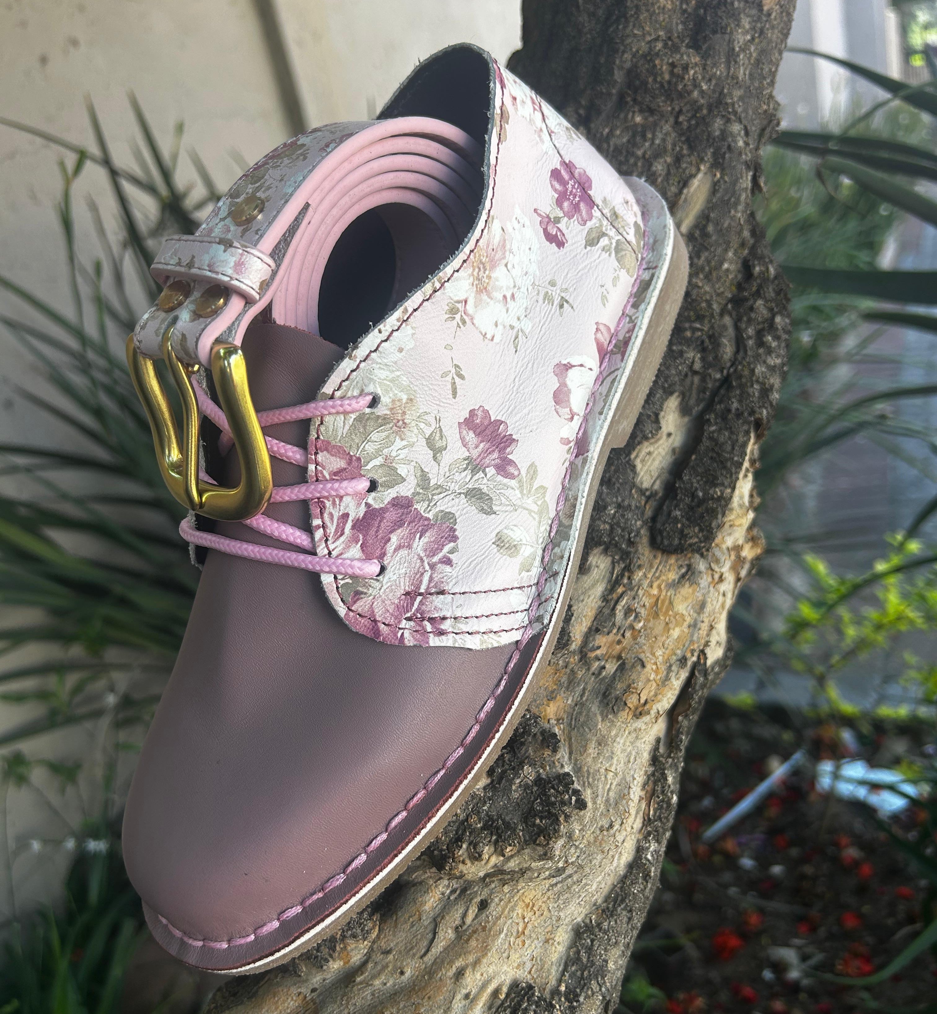 Floral-patterned shoe with pink laces on a tree branch