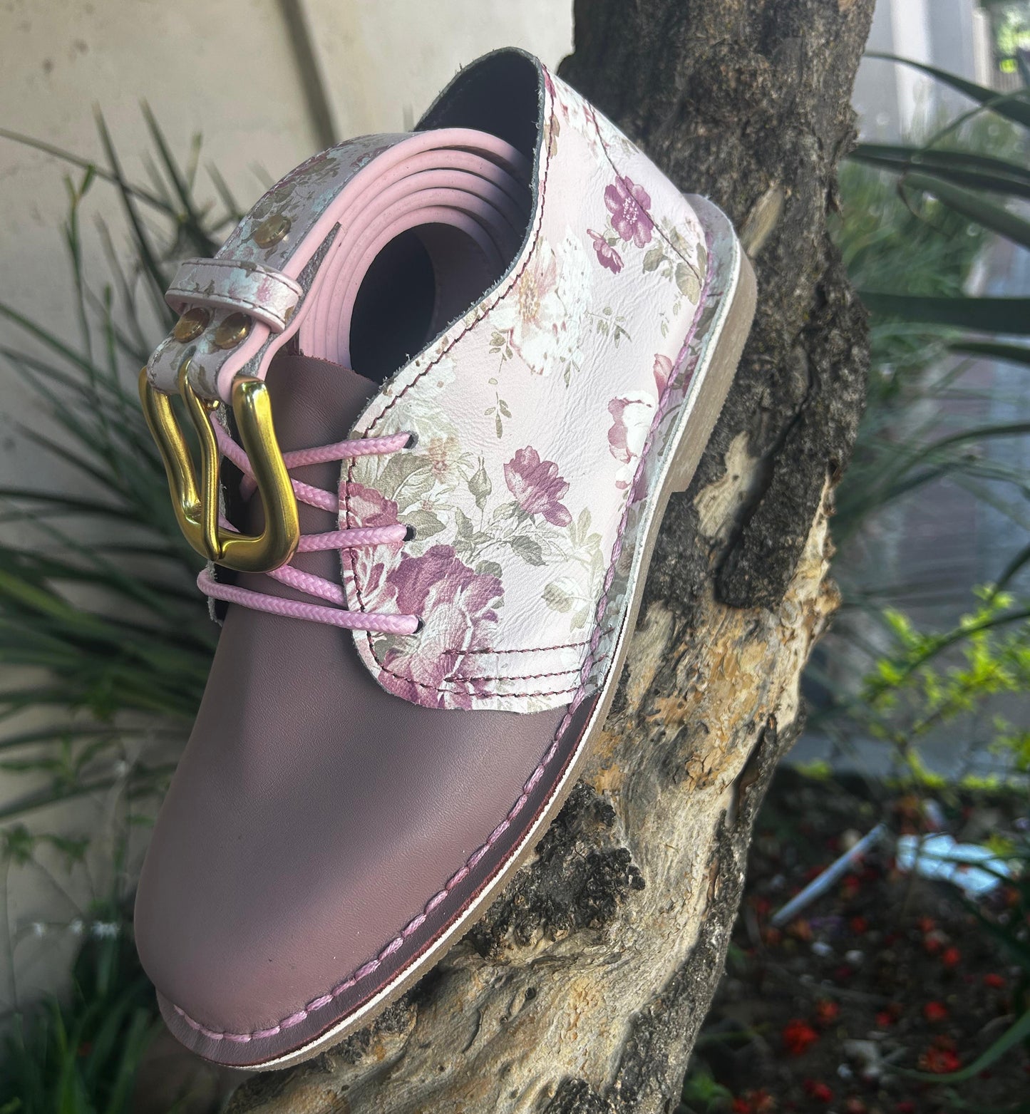 Floral-patterned shoe with pink laces on a tree branch
