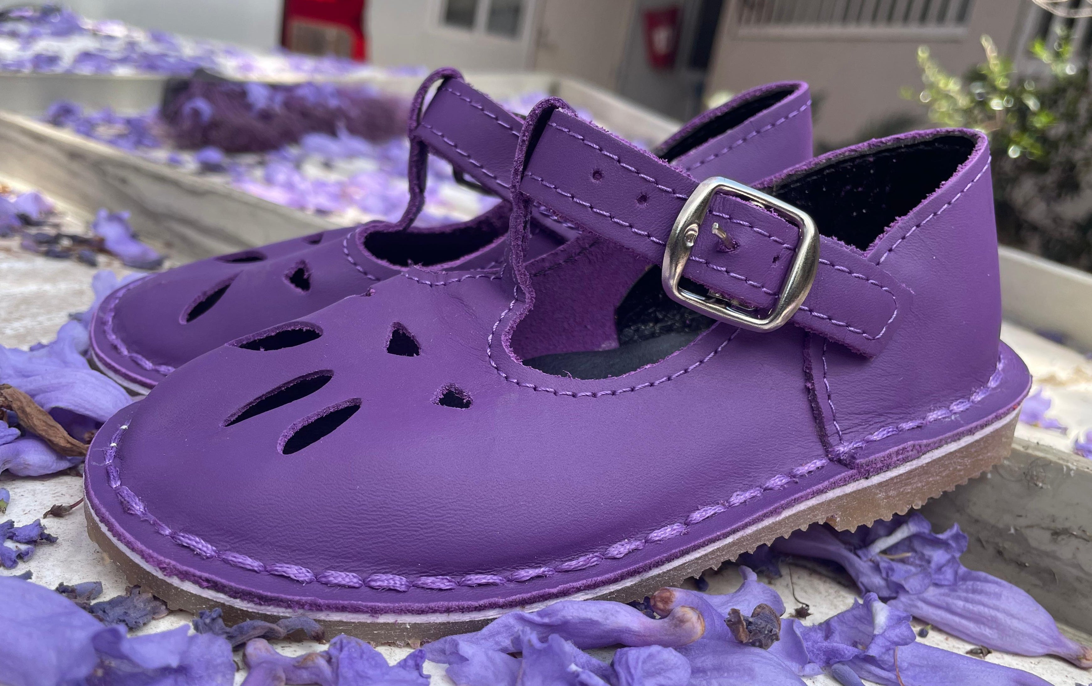 Purple children's shoes with a buckle on a surface with purple flowers.