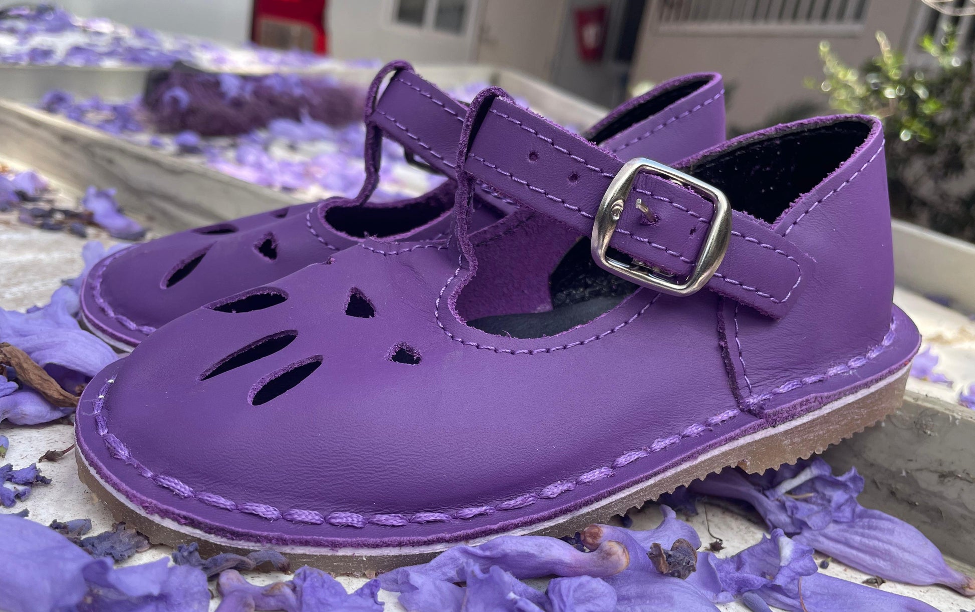 Purple children's shoes with a buckle on a surface with purple flowers.