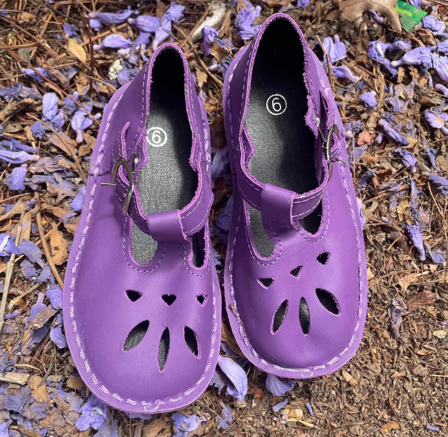 Purple children's shoes on a ground with purple flowers