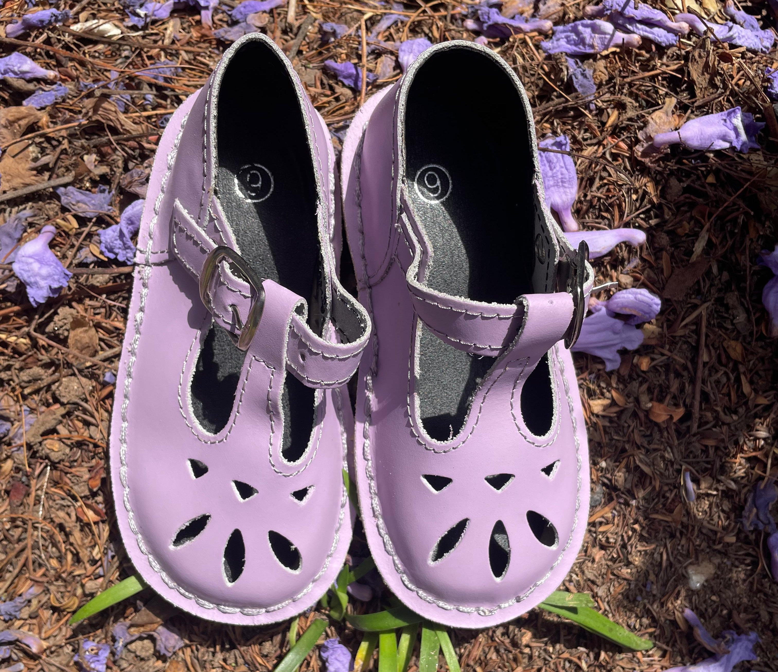 Pair of purple children's sandals on a ground with purple flowers